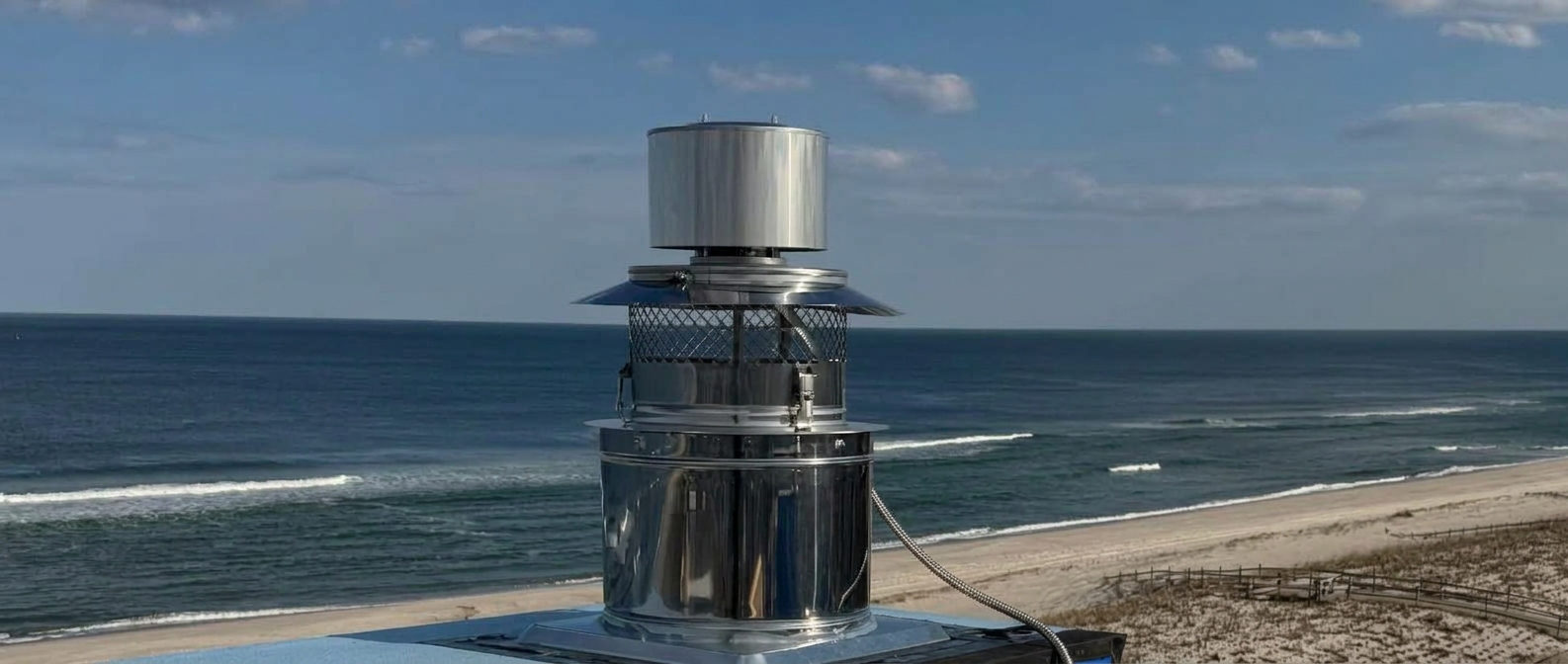 Stainless X-VENTISO draft inducer installed on a rooftop chimney overlooking the ocean